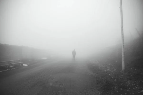 Man walking away on misty road. Man standing alone on rural foggy and misty asphalt road. Selective focus