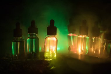 Vape kavramı. Sisli bir gecede dev cam şişe ile yolun ortasında duran bir adam silüeti elektronik sigara sıvı ile dolu. Işık arka plan üzerinde renkli sisli bulutlar.