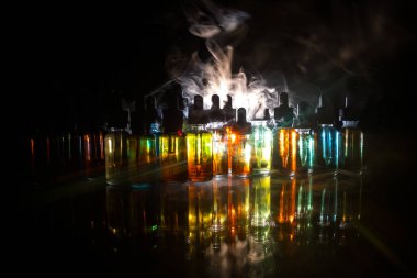 Vape kavramı. Duman bulutları ve vape sıvı şişe koyu arka plan üzerinde. Işık efektleri. Arka plan veya elektronik sigara reklam olarak kullanışlıdır. Seçici odak