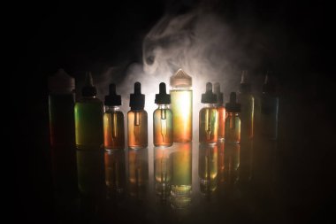Vape kavramı. Duman bulutları ve vape sıvı şişe koyu arka plan üzerinde. Işık efektleri. Arka plan veya elektronik sigara reklam olarak kullanışlıdır. Seçici odak