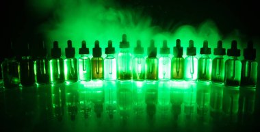 Vape kavramı. Duman bulutları ve vape sıvı şişe koyu arka plan üzerinde. Işık efektleri. Arka plan veya elektronik sigara reklam olarak kullanışlıdır. Seçici odak