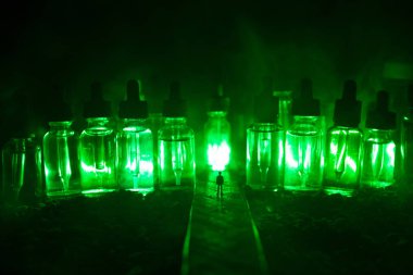 Vape kavramı. Sisli bir gecede dev cam şişe ile yolun ortasında duran bir adam silüeti elektronik sigara sıvı ile dolu. Işık arka plan üzerinde renkli sisli bulutlar.