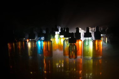 Vape kavramı. Duman bulutları ve vape sıvı şişe koyu arka plan üzerinde. Işık efektleri. Arka plan veya elektronik sigara reklam olarak kullanışlıdır. Seçici odak