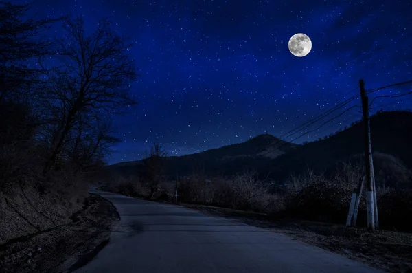 Mountain Road a través del bosque en una noche de luna llena. Paisaje nocturno escénico de carretera rural por la noche con luna grande. Fotografía del obturador largo — Foto de Stock