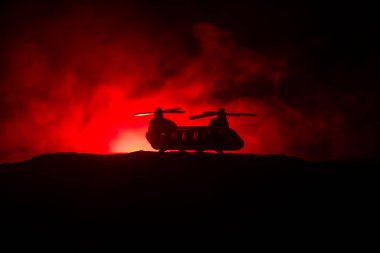 Askeri helikopterin silueti çatışma bölgesinden uçmaya hazır. Çölden başlayan sisli arka ışıklandırmalı helikopterle dekore edilmiş gece görüntüleri. Seçici odaklanma. Savaş konsepti