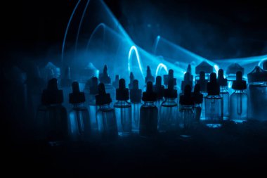 Vape kavramı. Duman bulutları ve vape sıvı şişe koyu arka plan üzerinde. Işık efektleri. Arka plan veya elektronik sigara reklam olarak kullanışlıdır. Seçici odak