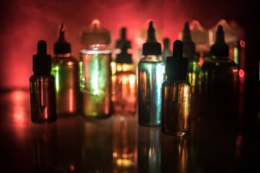 Vape kavramı. Duman bulutları ve vape sıvı şişe koyu arka plan üzerinde. Işık efektleri. Arka plan veya elektronik sigara reklam olarak kullanışlıdır. Seçici odak