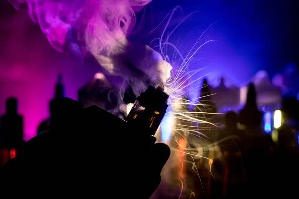 Vape concept. Electronic Cigarette vape explosion. Smoke clouds and vape liquid bottles on dark background. Light effects. Useful as vape advertisement. Selective focus