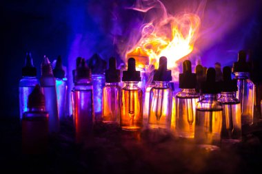 Vape kavramı. Duman bulutları ve vape sıvı şişe koyu arka plan üzerinde. Işık efektleri. Arka plan veya elektronik sigara reklam olarak kullanışlıdır. Seçici odak