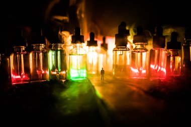 Vape kavramı. Sisli bir gecede dev cam şişe ile yolun ortasında duran bir adam silüeti elektronik sigara sıvı ile dolu. Işık arka plan üzerinde renkli sisli bulutlar.