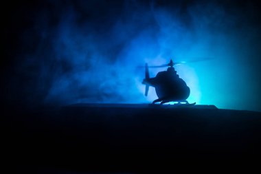 Askeri helikopterin silueti çatışma bölgesinden uçmaya hazır. Çölden başlayan sisli arka ışıklandırmalı helikopterle dekore edilmiş gece görüntüleri. Seçici odaklanma. Savaş konsepti
