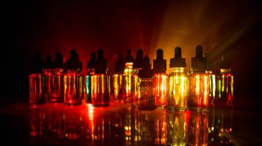 Vape kavramı. Duman bulutları ve vape sıvı şişe koyu arka plan üzerinde. Işık efektleri. Arka plan veya elektronik sigara reklam olarak kullanışlıdır. Seçici odak