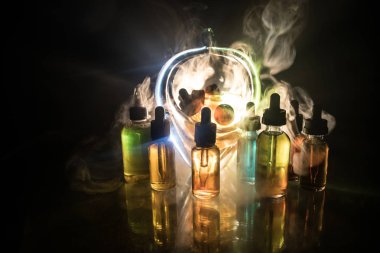 Vape kavramı. Duman bulutları ve vape sıvı şişe koyu arka plan üzerinde. Işık efektleri. Arka plan veya elektronik sigara reklam olarak kullanışlıdır. Seçici odak