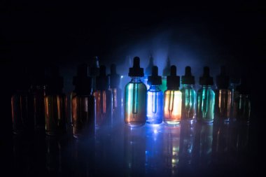 Vape kavramı. Duman bulutları ve vape sıvı şişe koyu arka plan üzerinde. Işık efektleri. Arka plan veya elektronik sigara reklam olarak kullanışlıdır. Seçici odak