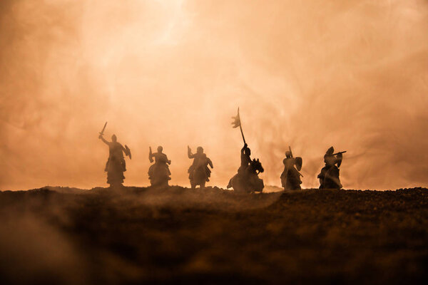 Medieval battle scene with cavalry and infantry. Silhouettes of figures as separate objects, fight between warriors on sunset foggy background. Selective focus