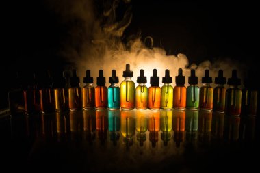 Vape kavramı. Duman bulutları ve vape sıvı şişe koyu arka plan üzerinde. Işık efektleri. Arka plan veya elektronik sigara reklam olarak kullanışlıdır. Seçici odak