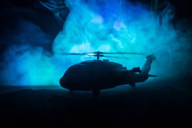 Askeri helikopterin silueti çatışma bölgesinden uçmaya hazır. Çölden başlayan sisli arka ışıklandırmalı helikopterle dekore edilmiş gece görüntüleri. Seçici odaklanma. Savaş konsepti