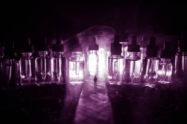 Vape kavramı. Sisli bir gecede dev cam şişe ile yolun ortasında duran bir adam silüeti elektronik sigara sıvı ile dolu. Işık arka plan üzerinde renkli sisli bulutlar.