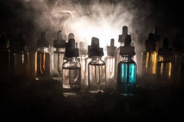 Vape kavramı. Duman bulutları ve vape sıvı şişe koyu arka plan üzerinde. Işık efektleri. Arka plan veya elektronik sigara reklam olarak kullanışlıdır. Seçici odak