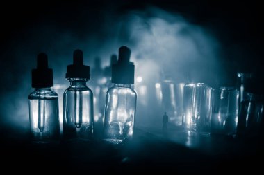Vape kavramı. Sisli bir gecede dev cam şişe ile yolun ortasında duran bir adam silüeti elektronik sigara sıvı ile dolu. Işık arka plan üzerinde renkli sisli bulutlar.