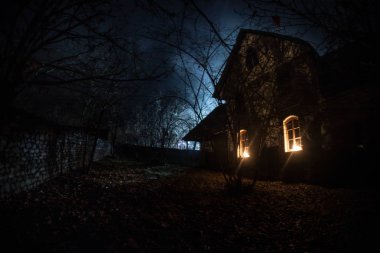 Geceleri ormanda bir hayaletin olduğu eski bir ev ya da sis içinde terk edilmiş bir korku evi. Ölü ağaç ormanındaki eski mistik bina. Geceleri aylı ağaçlar. Gerçeküstü ışıklar. Korku Cadılar Bayramı konsepti