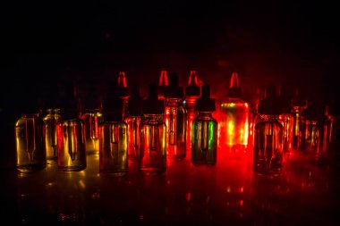 Vape kavramı. Duman bulutları ve vape sıvı şişe koyu arka plan üzerinde. Işık efektleri. Arka plan veya elektronik sigara reklam olarak kullanışlıdır. Seçici odak