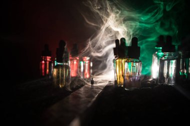 Vape kavramı. Sisli bir gecede dev cam şişe ile yolun ortasında duran bir adam silüeti elektronik sigara sıvı ile dolu. Işık arka plan üzerinde renkli sisli bulutlar.