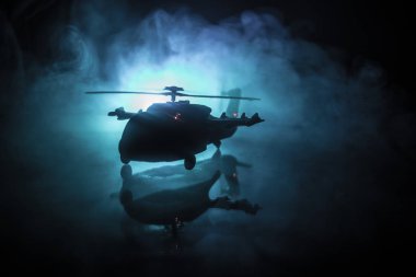 Askeri helikopterin silueti çatışma bölgesinden uçmaya hazır. Çölden başlayan sisli arka ışıklandırmalı helikopterle dekore edilmiş gece görüntüleri. Seçici odaklanma. Savaş konsepti