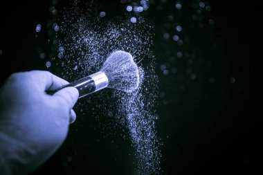 Makyaj, ışık ve duman ile koyu arka plan üzerinde kozmetik toz el fırça. Karanlık toz sıçrama