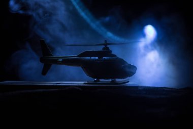 Askeri helikopterin silueti çatışma bölgesinden uçmaya hazır. Çölden başlayan sisli arka ışıklandırmalı helikopterle dekore edilmiş gece görüntüleri. Seçici odaklanma. Savaş konsepti