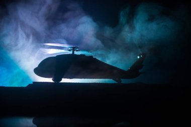 Askeri helikopterin silueti çatışma bölgesinden uçmaya hazır. Çölden başlayan sisli arka ışıklandırmalı helikopterle dekore edilmiş gece görüntüleri. Seçici odaklanma. Savaş konsepti