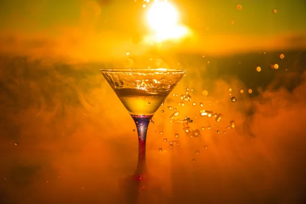 马提尼鸡尾酒玻璃飞溅在雾蒙蒙的日落背景或五颜六色的鸡尾酒在玻璃与飞溅和柠檬 户外露天派对娱乐 选择性对焦 — 图库照片