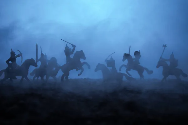 Medieval battle scene with cavalry and infantry. Silhouettes of figures as separate objects, fight between warriors on sunset foggy background. Selective focus — Stock Photo, Image