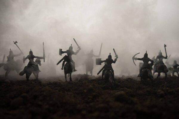Medieval battle scene with cavalry and infantry. Silhouettes of figures as separate objects, fight between warriors on sunset foggy background. Selective focus