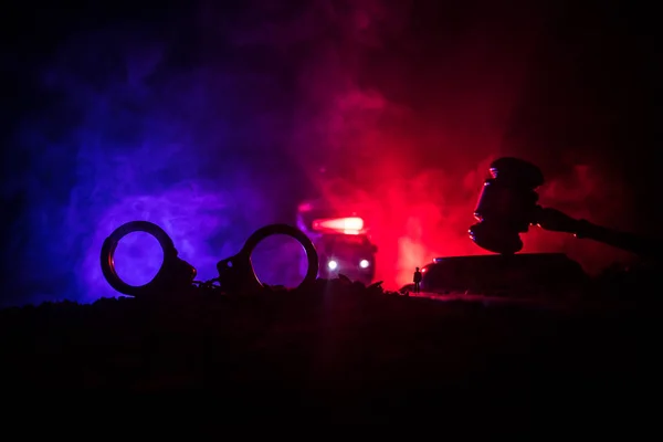 Έννοια νομικού δικαίου. Σιλουέτα χειροπέδες με το άγαλμα της δικαιοσύνης στην πίσω πλευρά με τα λαμπερά φώτα κόκκινα και μπλε αστυνομία στο ομιχλώδες φόντο. Επιλεκτική εστίαση — Φωτογραφία Αρχείου