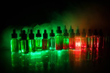 Vape kavramı. Duman bulutları ve vape sıvı şişe koyu arka plan üzerinde. Işık efektleri. Arka plan veya elektronik sigara reklam olarak kullanışlıdır. Seçici odak