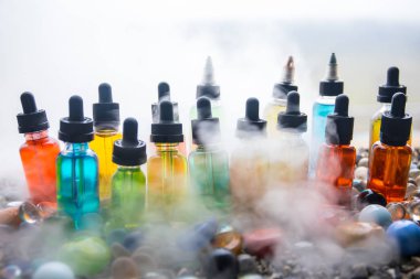 Vape kavramı. Güzel renkli vape sıvı cam şişeler taşlar hakkında açık. Arka plan veya elektronik sigara reklam olarak kullanışlıdır. Seçici odak