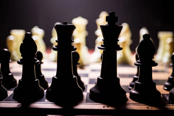 Schackbräde spel begreppet affärsidéer och konkurrens. Schack figurer på en mörk bakgrund med rök och dimma. — Stockfoto