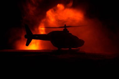 Askeri helikopterin silueti çatışma bölgesinden uçmaya hazır. Çölden başlayan sisli arka ışıklandırmalı helikopterle dekore edilmiş gece görüntüleri. Seçici odaklanma. Savaş konsepti