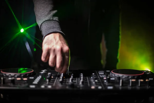 DJ Spinning, Mixing, and Scratching in a Night Club, Hands of dj tweak various track controls on dj's deck, strobe lights and fog, or Dj mixes the track in the nightclub at party. Selective focus