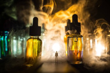 Vape kavramı. Sisli bir gecede dev cam şişe ile yolun ortasında duran bir adam silüeti elektronik sigara sıvı ile dolu. Işık arka plan üzerinde renkli sisli bulutlar.