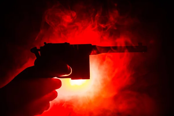 男性手拿着枪在黑色背景与烟雾色调后灯 — 图库照片