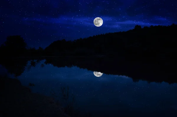 Esta espectacular salida de la luna en un cielo nocturno azul profundo está acentuada por las nubes resaltadas y la hermosa y tranquila reflexión del lago. — Foto de Stock