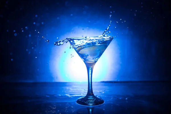 Martini-Cocktailglas in der Hand, das auf dunklem rauchigen Hintergrund plätschert, oder bunter Cocktail im Glas mit Spritzern und Oliven. Party Club Unterhaltung. gemischtes Licht. Selektiver Fokus — Stockfoto