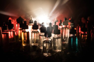 Vape kavramı. Duman bulutlar ve karanlık arka plan üzerinde vape sıvı şişeler. Işık efektleri. Arka plan veya elektronik sigara reklamı olarak kullanışlı.