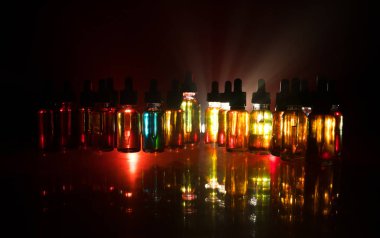 Vape kavramı. Duman bulutlar ve karanlık arka plan üzerinde vape sıvı şişeler. Işık efektleri. Arka plan veya elektronik sigara reklamı olarak kullanışlı.