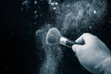 Makyaj, ışık ve duman ile koyu arka plan üzerinde kozmetik toz el fırça. Karanlık toz sıçrama