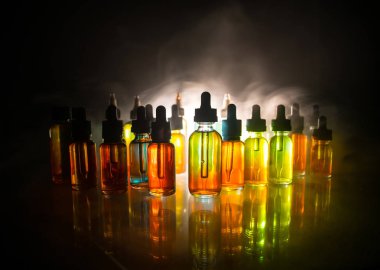 Vape kavramı. Duman bulutlar ve karanlık arka plan üzerinde vape sıvı şişeler. Işık efektleri. Arka plan veya elektronik sigara reklamı olarak kullanışlı.