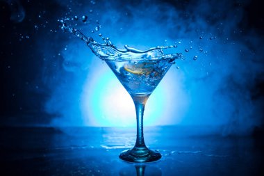 Martini kokteyl cam el koyu tonda dumanlı arka plan veya renkli kokteyl cam su sıçramalarına ve zeytin sıçramasına. Parti club eğlence. Karışık ışık. Seçici odak