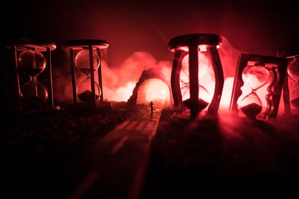Koncepcja czasu. Sylwetka mężczyzny stojącego między klepsydrami z dymem i światłami na ciemnym tle. Surrealistyczne dekorowane zdjęcie — Zdjęcie stockowe